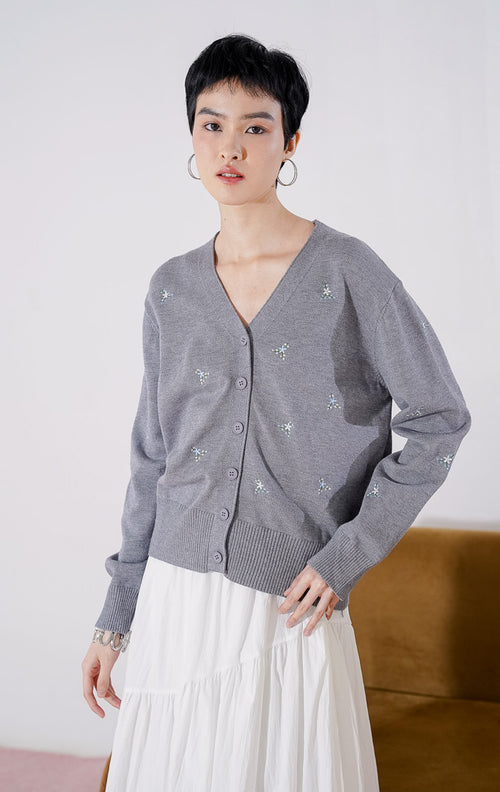 Tampak depan This Is April Petunia Cardigan warna abu-abu, berupa cardigan rajut lengan panjang kerah V-neck dengan kancing depan dan detail motif bordir bunga kecil yang tersebar.