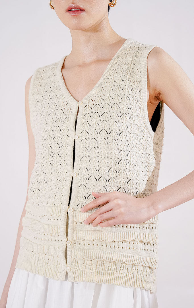 Tampak depan This Is April Pierre Vest warna ivory, rompi rajut crochet tanpa lengan dengan pola rajutan kait bertekstur, kerah V-neck, dan kancing depan