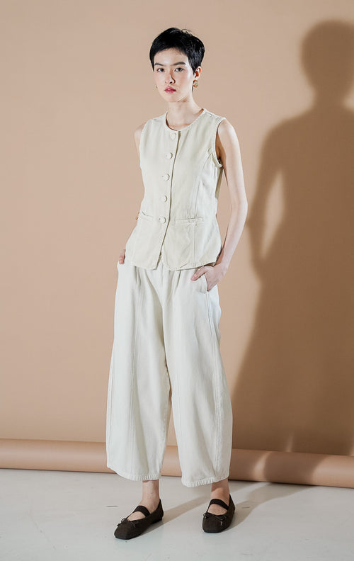 Rielle Vest Ivory dari This Is April, rompi denim tanpa lengan warna putih gading dengan kancing depan senada, kerah bulat, dan dua saku fungsional di bagian depan.