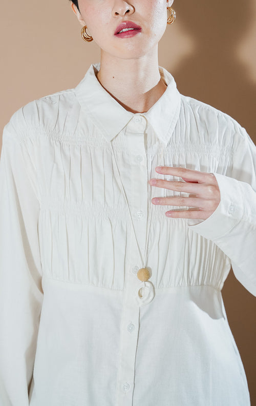 Valuna Top White dari This Is April, kemeja katun lengan panjang warna putih dengan detail kerutan (smocked texture) pada bagian dada dan kancing depan.