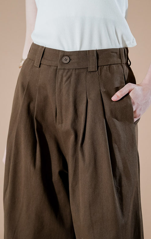 Yuriku Pants Dark Brown dari This Is April, celana panjang kulot wide-leg wanita warna cokelat tua dengan detail lipit depan (pleated) dan bahan katun terstruktur.