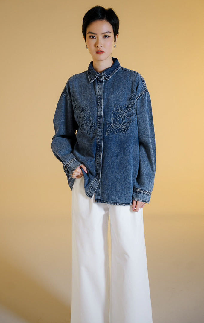 Pakaian wanita model kemeja jeans lengan panjang dengan detail bordir kontur bunga (floral contour embroidered denim shirt) warna biru denim Aevia Top untuk gaya kasual anggun. 