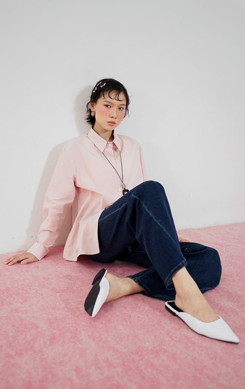 Model wanita mengenakan kemeja lengan panjang katun This Is April Athena Top warna light pink dengan kancing depan, dipadukan dengan celana jeans panjang biru tua, kalung aksesoris, dan sepatu putih.