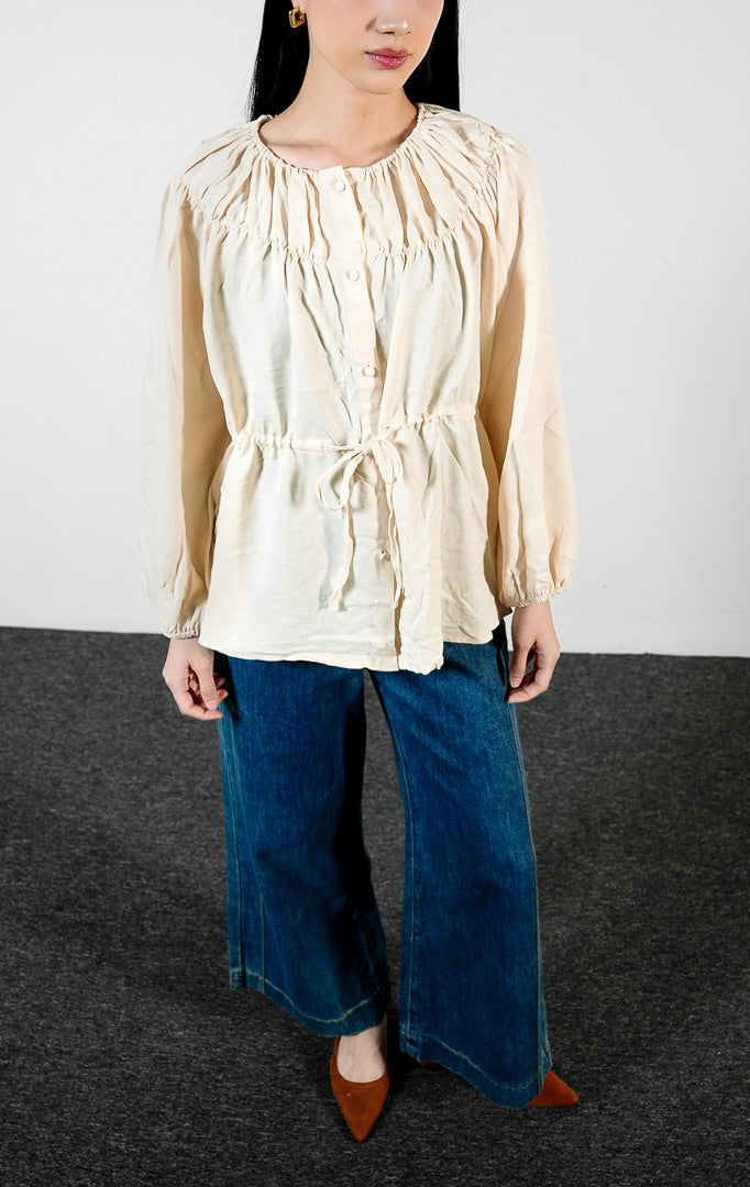 Pakaian wanita model blouse lengan panjang berkerut dengan detail tali serut pinggang dan kerah bahu terbuka (off-the-shoulder yoke blouse) warna ivory Avelyn Top untuk gaya kasual chic.