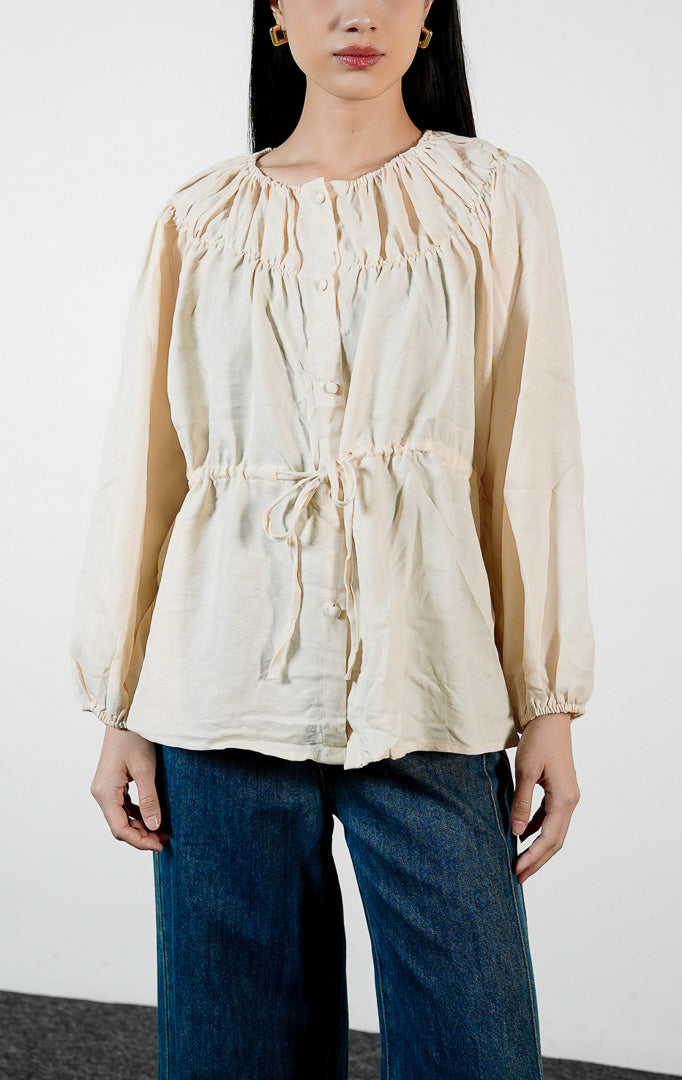 Pakaian wanita model blouse lengan panjang berkerut dengan detail tali serut pinggang dan kerah bahu terbuka (off-the-shoulder yoke blouse) warna ivory Avelyn Top untuk gaya kasual chic.