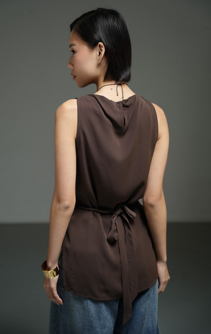 Atasan wanita tanpa lengan warna cokelat tua (dark brown knot detail boat neck top) Cassey Top dengan model leher perahu yang anggun, aksen lilitan simpul yang unik, serta potongan belahan bawah modern. 