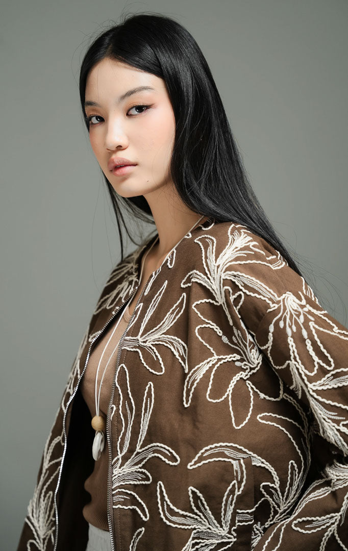 Jaket wanita lengan panjang warna cokelat tua (dark brown embroidered floral jacket) Catharina Jacket dengan detail bordir motif bunga putih yang rumit, bahan katun berpori yang nyaman, serta resleting depan.