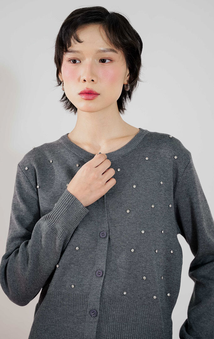 Model mengenakan This Is April Daimen Cardigan Grey, knit cardigan abu-abu dengan detail manik-manik rhinestone dan celana putih.