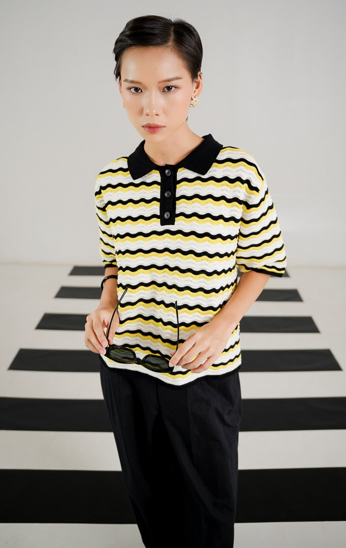 Atasan rajut wanita lengan pendek bermotif garis gelombang (wavy) perpaduan warna kuning, putih, dan hitam, dilengkapi kerah polo hitam dan kancing depan dari This Is April. 