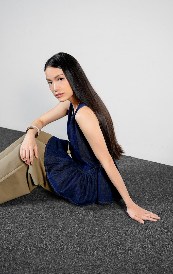 Atasan wanita model peplum tanpa lengan bahan denim warna dark denim dengan potongan pinggang rendah yang terstruktur (dark denim sculpted drop-waist peplum top) Emalyne Top untuk gaya feminin modern.