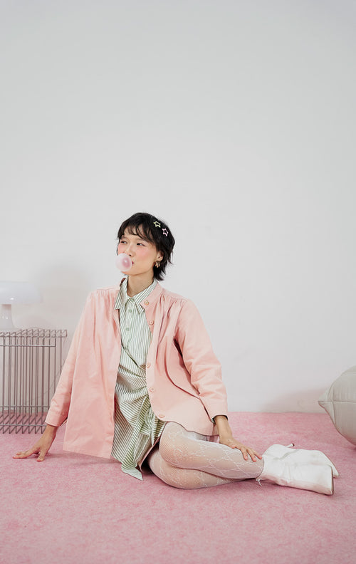 Model mengenakan This Is April Emory Top Dusty Pink, kemeja lengan panjang wanita bahan katun warna dusty pink dengan detail kancing emas di bagian depan.