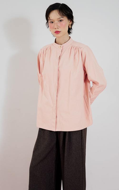Model mengenakan This Is April Emory Top Dusty Pink, kemeja lengan panjang wanita bahan katun warna dusty pink dengan detail kancing emas di bagian depan.