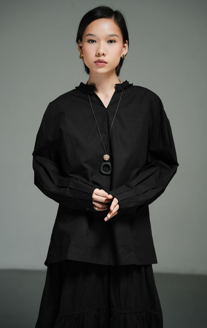 Blus wanita lengan panjang warna hitam (black pleated-trim stand collar blouse) Florina Top dengan bahan katun poplin berkualitas, kerah tegak berdetail lipatan plisket, serta potongan siluet modern yang tegas. 