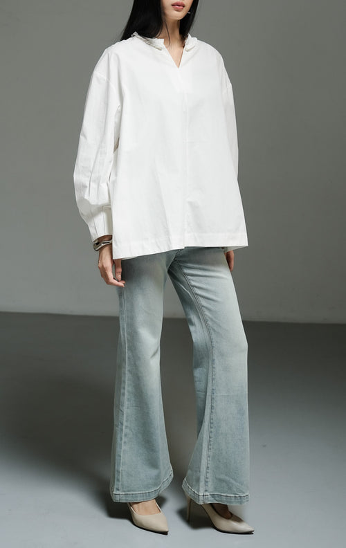 Blus wanita lengan panjang warna putih (white pleated-trim stand collar blouse) Florina Top dengan bahan katun poplin klasik berstruktur, kerah tegak beraksen trim plisket, serta siluet longgar yang bersih. 