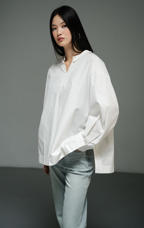 Blus wanita lengan panjang warna putih (white pleated-trim stand collar blouse) Florina Top dengan bahan katun poplin klasik berstruktur, kerah tegak beraksen trim plisket, serta siluet longgar yang bersih. 