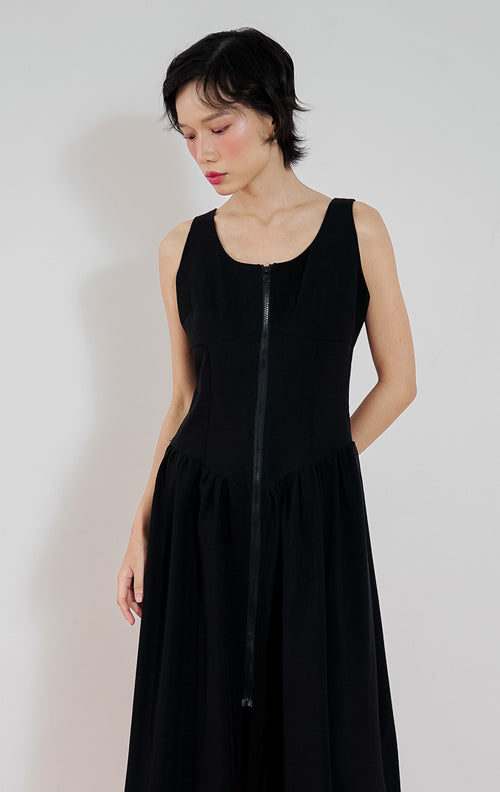 Model mengenakan gaun hitam tanpa lengan This Is April Giorgi Dress dengan detail resleting depan (zipper) dan potongan pinggang rendah (drop-waist) yang mengembang.