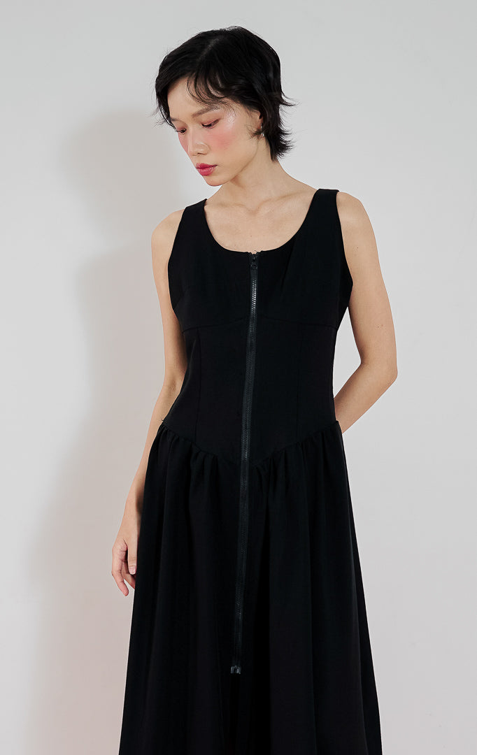 Model mengenakan gaun hitam tanpa lengan This Is April Giorgi Dress dengan detail resleting depan (zipper) dan potongan pinggang rendah (drop-waist) yang mengembang.