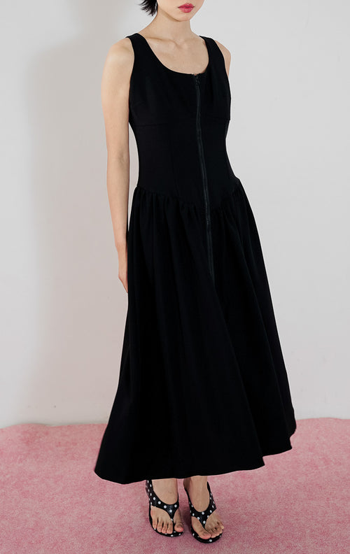 Model mengenakan gaun hitam tanpa lengan This Is April Giorgi Dress dengan detail resleting depan (zipper) dan potongan pinggang rendah (drop-waist) yang mengembang.