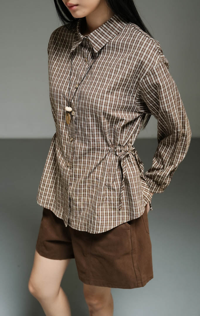 Kemeja wanita lengan panjang motif kotak-kotak warna cokelat (brown plaid drawstring shirt top) Hilaria Top dengan bahan katun non-stretch berkualitas, penutup kancing depan, serta tali serut pinggang untuk siluet yang ramping dan rapi. 