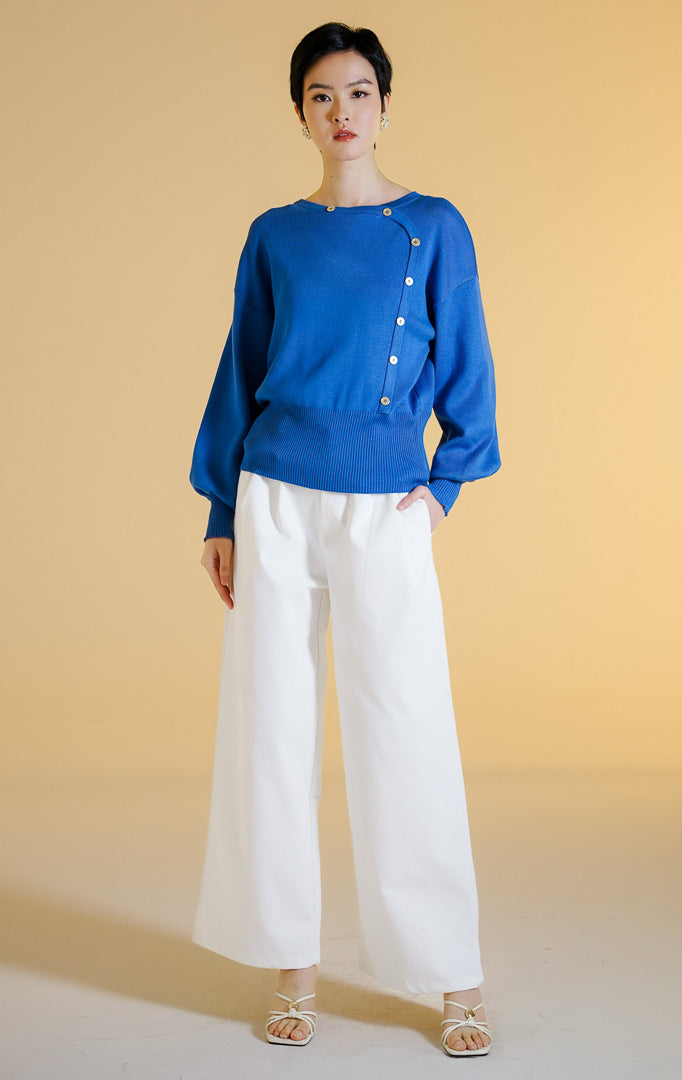 Pakaian hangat wanita model sweter rajut lengan panjang dengan potongan asimetris dan aksen kancing emas (asymmetrical gold button knit sweater) warna biru Ismeria Sweater untuk gaya kantor dan kasual anggun. 
