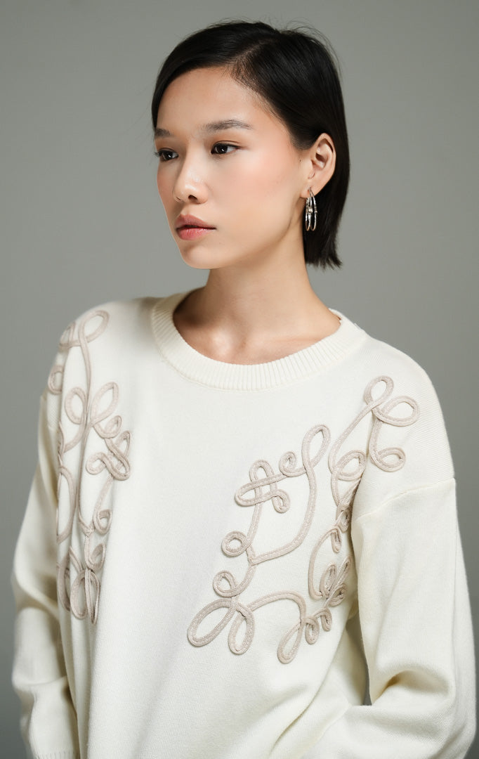 Atasan wanita model sweater rajut warna ivory dengan detail bordir tali bermotif bunga (ivory floral cord embroidery knit sweater) Jenny Sweater untuk tampilan kasual yang anggun. 