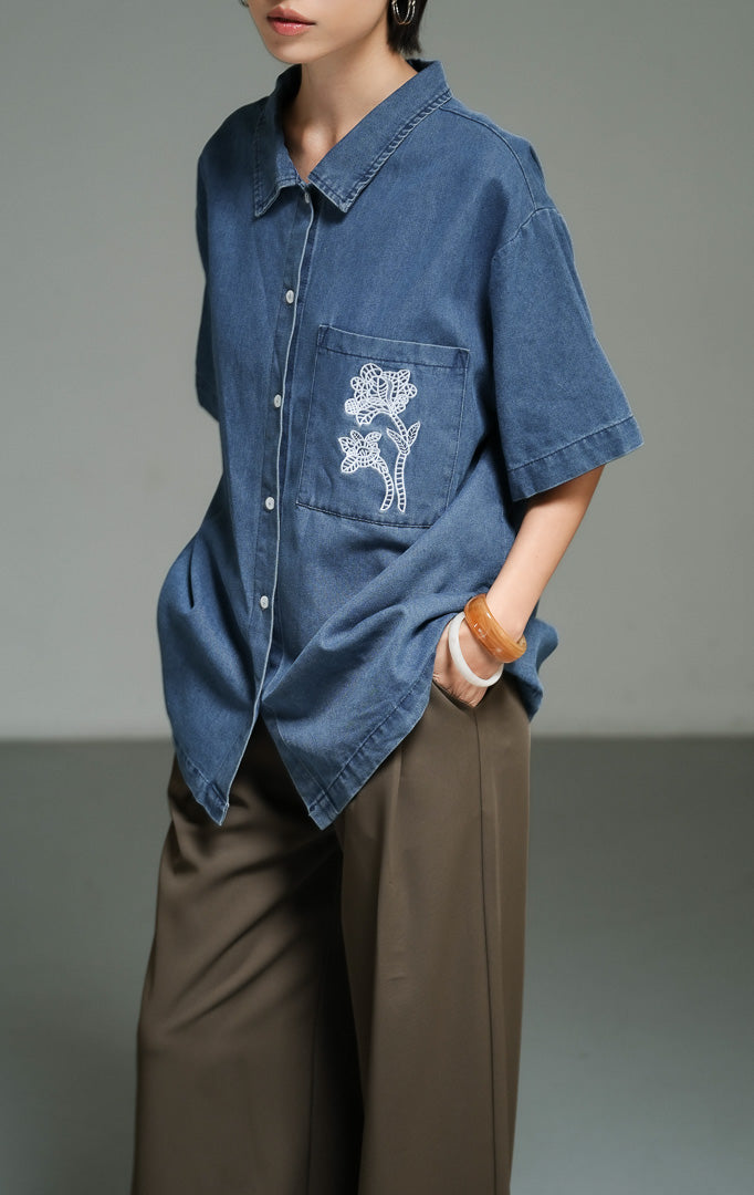 Atasan wanita model kemeja denim lengan pendek warna dark denim dengan detail bordir renda bunga pada bagian saku (dark denim floral lace embroidery shirt top) Kaelina Top yang gaya dan kasual