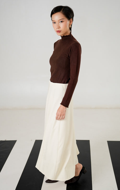 Rok midi wanita (midi skirt) warna cream (krem) berpotongan rapi dengan detail jahitan panel lurus dan resleting (zipper) tersembunyi dari This Is April. 