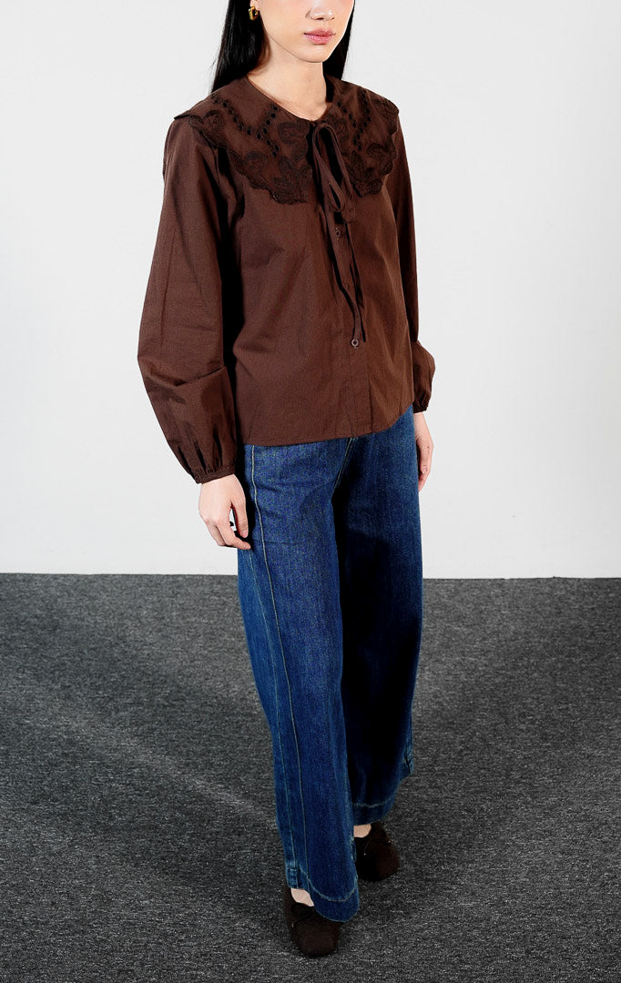Pakaian wanita model blouse lengan panjang bahan katun dengan detail kerah bordir motif lubang (eyelet broderie) dan tepi gelombang (scalloped edges) warna cokelat tua Lioren Top untuk gaya kasual anggun. 