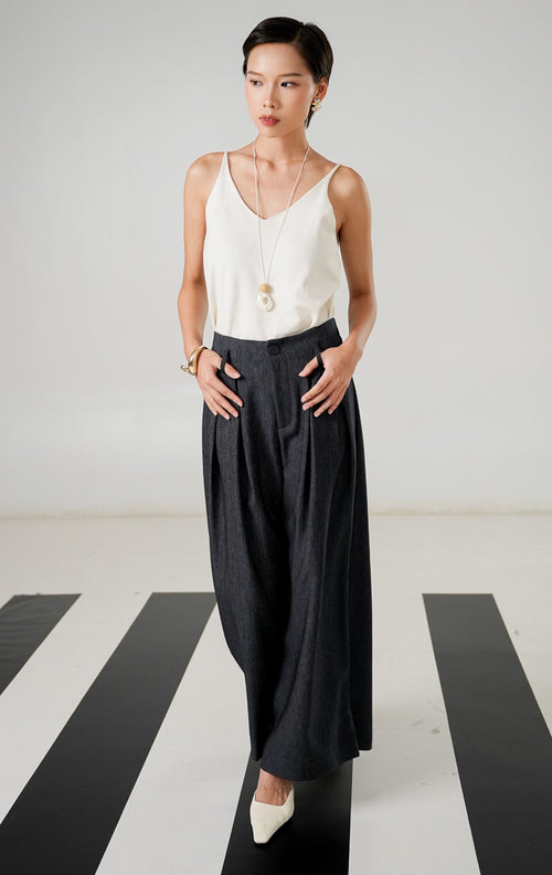 Celana panjang wanita berpotongan lebar (wide leg) warna abu abu tua (dark grey) dengan detail kancing depan, resleting, lipatan (pleats), dan pinggang karet dari This Is April. 