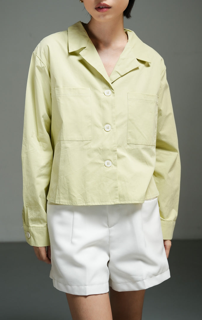 Atasan wanita model blazer pendek (cropped blazer top) warna hijau sage (green Cuban collar cropped blazer) Meadow Top dengan detail kerah Kuba, bahan katun berstruktur non-stretch, serta kancing depan penuh.