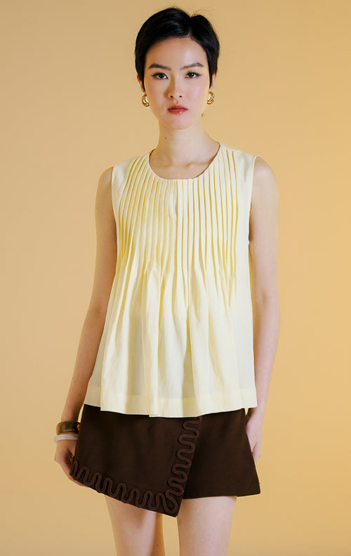 Pakaian wanita model atasan tanpa lengan kerah bulat dengan detail lipit vertikal dan bagian bawah mengembang (pleated sleeveless top) warna kuning lembut Butter Yellow Miuza Top untuk gaya kasual anggun. 