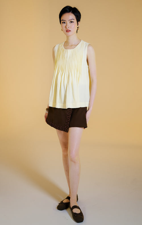Pakaian wanita model atasan tanpa lengan kerah bulat dengan detail lipit vertikal dan bagian bawah mengembang (pleated sleeveless top) warna kuning lembut Butter Yellow Miuza Top untuk gaya kasual anggun. 