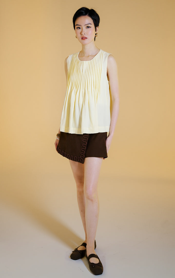 Pakaian wanita model atasan tanpa lengan kerah bulat dengan detail lipit vertikal dan bagian bawah mengembang (pleated sleeveless top) warna kuning lembut Butter Yellow Miuza Top untuk gaya kasual anggun. 