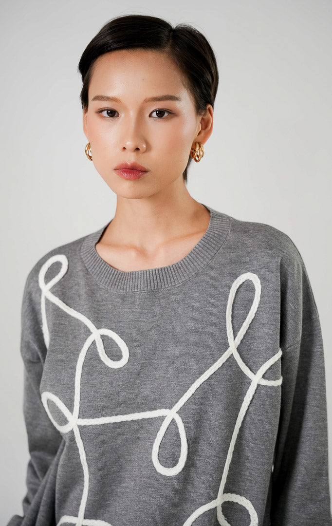 Sweater rajut wanita lengan panjang warna abu abu (grey) dengan detail bordir garis lengkung abstrak berwarna putih di bagian depan dari This Is April. 