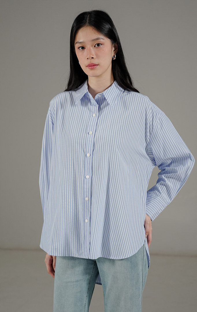 Olivier Top Light Blue dari This Is April, kemeja oversize motif salur vertikal biru putih dengan potongan asimetris dan kancing depan.