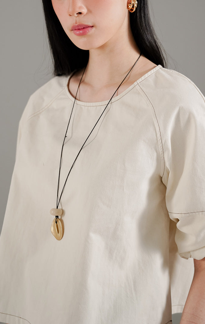 Quincy Top Ivory dari This Is April, atasan lengan panjang wanita warna putih gading dengan detail jahitan cokelat kontras di seluruh siluet dan pergelangan tangan karet.