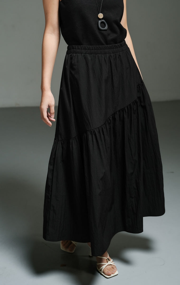 Rok panjang wanita model maxi asimetris warna hitam (black asymmetric gathered maxi skirt) Riami Skirt dengan desain potongan miring yang modern, detail kerut bertingkat yang anggun, serta siluet kasual berkelas. 