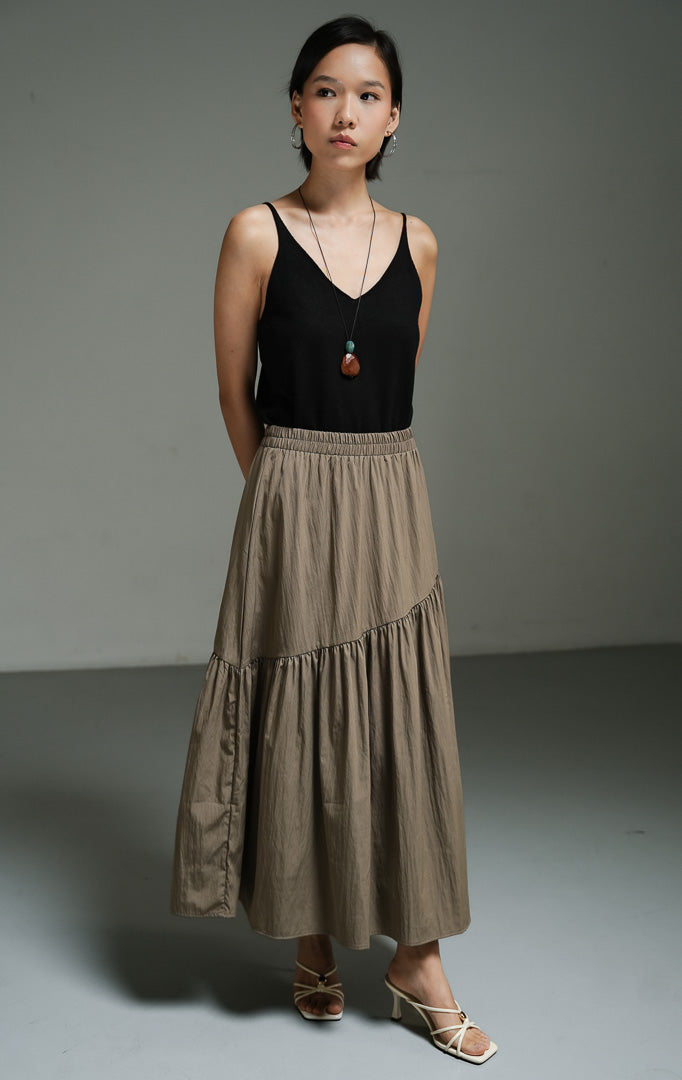 Rok panjang wanita model maxi asimetris warna taupe (taupe asymmetric gathered maxi skirt) Riami Skirt dengan detail potongan miring, bahan campuran katun-poliester berkualitas, serta kerut fluid yang elegan. 