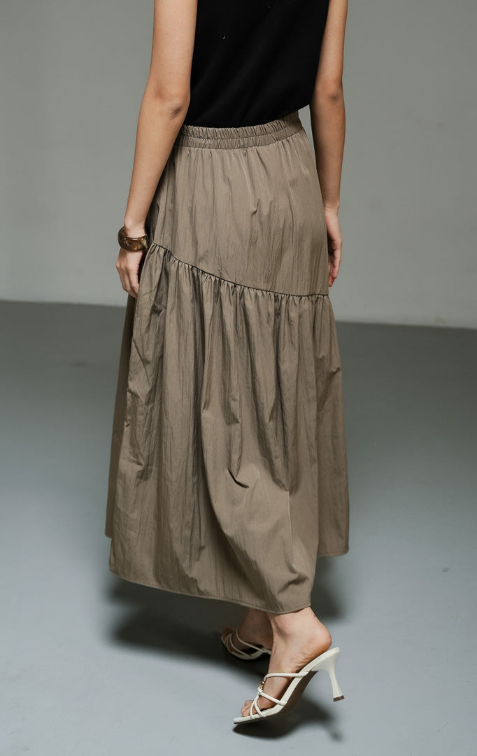 Rok panjang wanita model maxi asimetris warna taupe (taupe asymmetric gathered maxi skirt) Riami Skirt dengan detail potongan miring, bahan campuran katun-poliester berkualitas, serta kerut fluid yang elegan. 