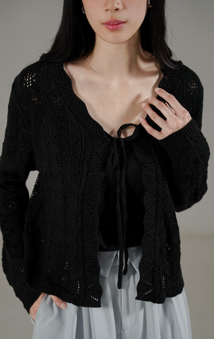  Robbie Cardigan Black dari This Is April, outer rajut berongga warna hitam dengan detail tali depan dan pinggiran bergelombang (scalloped edge).