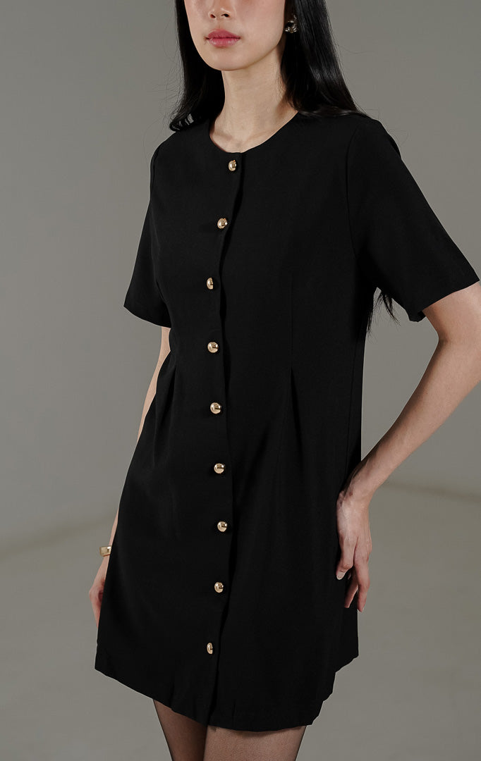 Rolaine Dress Black dari This Is April, gaun pendek warna hitam dengan detail kancing emas aktif di bagian depan bergaya mewah