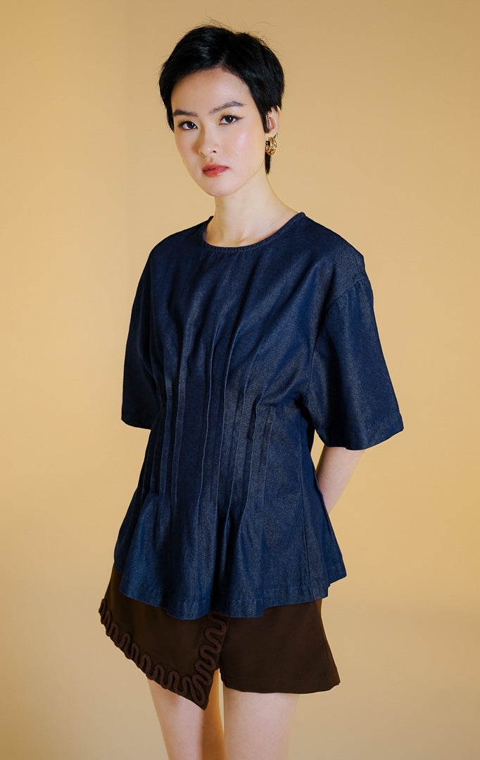 Pakaian wanita model atasan bahan denim lengan pendek dengan detail lipit pinggang ala korset (corset-inspired pleated denim top) warna dark denim Solviera Top untuk gaya kasual elegan. 