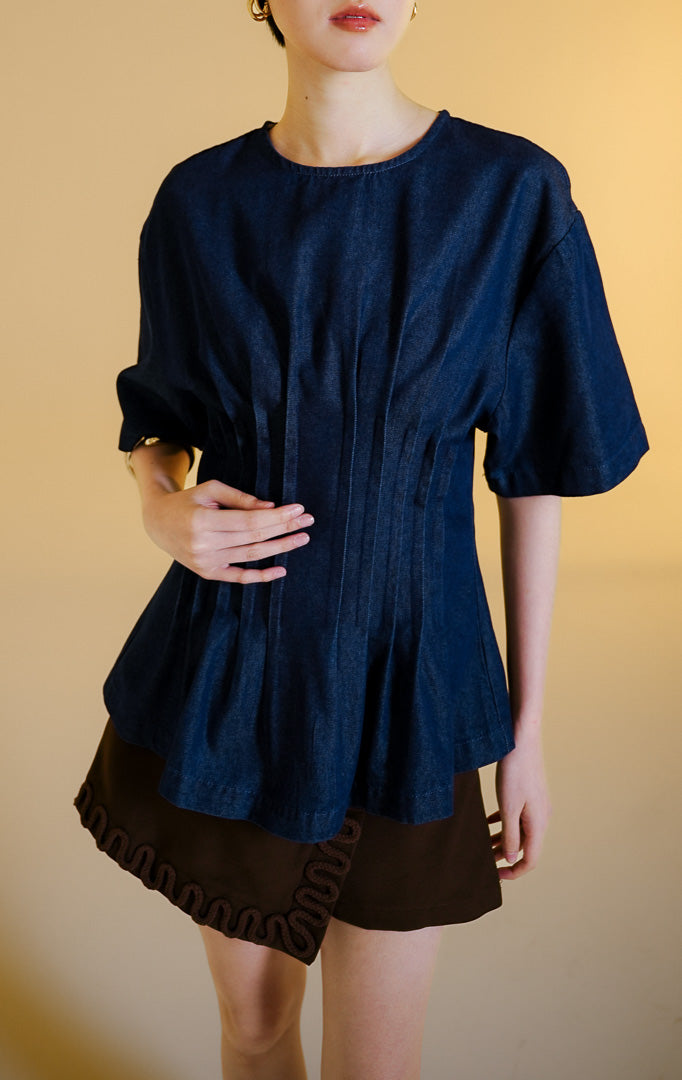 Pakaian wanita model atasan bahan denim lengan pendek dengan detail lipit pinggang ala korset (corset-inspired pleated denim top) warna dark denim Solviera Top untuk gaya kasual elegan. 