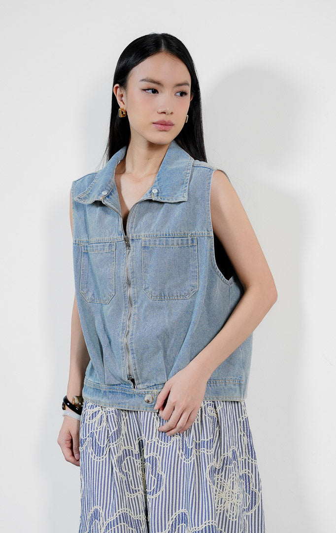 Pakaian wanita model rompi denim tanpa lengan warna biru muda (light denim vest) dengan detail saku tempel ganda, resleting, dan kerah rajut crochet tambahan Trixie Vest untuk gaya kasual modern yang unik. 