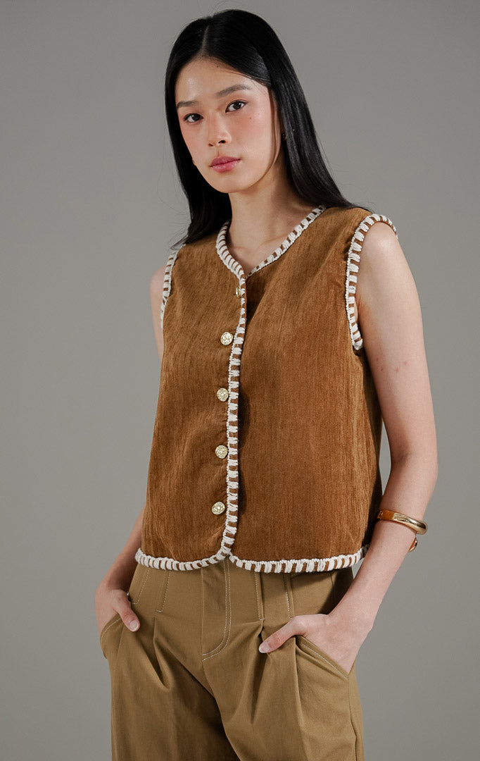 Vesta Vest Brown dari This Is April, rompi tanpa lengan warna cokelat mustard dengan detail jahitan tepi warna putih dan kancing emas.