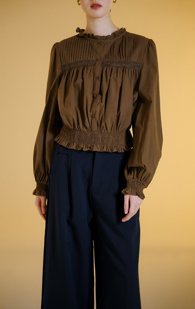 Pakaian wanita model blouse katun lengan panjang dengan detail lipit pada bagian dada dan potongan peplum (pin-tucked peplum blouse) warna cokelat tua Violetta Top untuk gaya kasual anggun. 