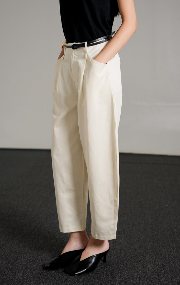 Timmy Pants Ivory, celana katun panjang warna putih gading dengan potongan barrel-leg yang melengkung unik, dipadukan dengan tank top hitam.