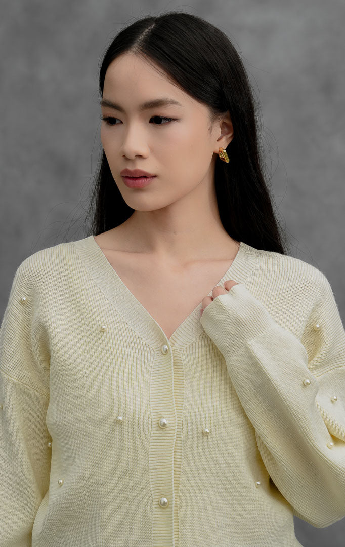 Kardigan rajut wanita lengan panjang warna ivory Vanessa Cardigan dengan kerah V (V-neck), bukaan kancing depan, dan aksen hiasan mutiara (scattered pearl details).