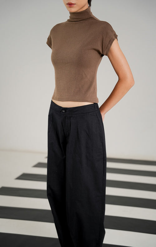 Celana panjang bahan katun wanita Veilon Pants Black dengan detail kancing di ujung kaki (buttoned hem), ban pinggang elastis di bagian belakang, dan aksen lipit depan (pleats). 