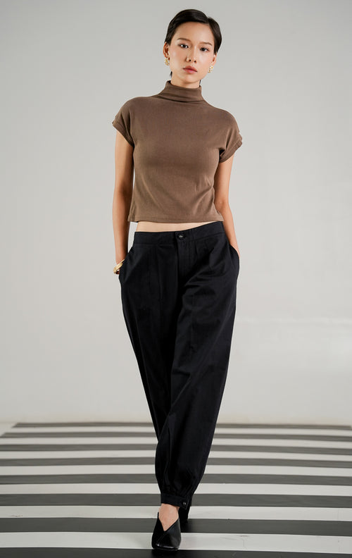 Celana panjang bahan katun wanita Veilon Pants Black dengan detail kancing di ujung kaki (buttoned hem), ban pinggang elastis di bagian belakang, dan aksen lipit depan (pleats). 